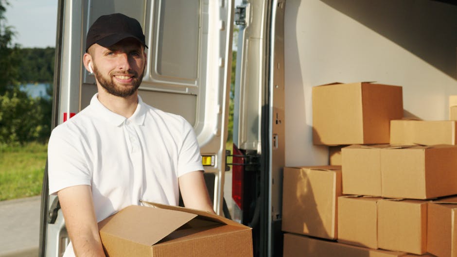 A man dressed in a blue long-sleeved shirt, black padded vest, and black trousers, wearing white sneakers and a grey cap, standing outside a residential property next to a white moving van with a wood