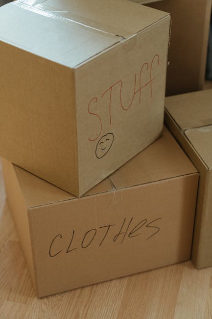 Close-up view of three brown cardboard boxes stacked inside a property, with the top box labeled 'STUFF' in red marker and featuring a small smiley face, and the lower box labeled 'CLOTHES' also handw